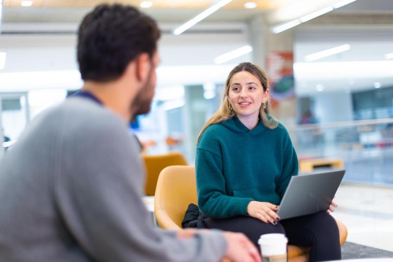 student chatting with another student with a laptop in her lap